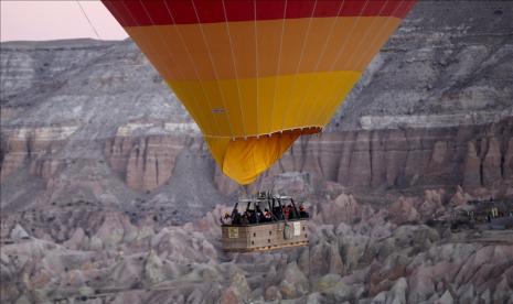 Balon udara melayang di atas wilayah Cappadocia yang bersejarah, di provinsi Nevsehir, Anatolia Tengah, Turki pada 5 Januari 2021. Cappadocia dilestarikan sebagai situs Warisan Dunia UNESCO, terkenal dengan bebatuan cerobong asapnya, wisata balon udara, kota bawah tanah dan hotel butik yang diukir dari batu. Sebagai salah satu kawasan pariwisata terpenting di Turki, wisatawan lokal dan asing bisa menikmati pemandangan, menaiki balon udara, menunggang kuda dan unta, hingga berjalan di antara cerobong peri. 