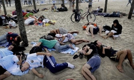 Beberapa orang tidur nyenyak di pasir pinggir pantai.