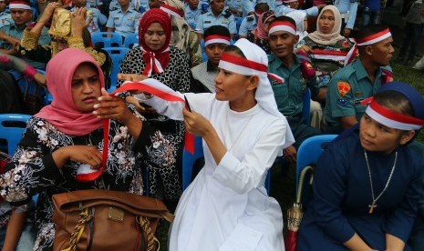 Nuns help pair a red and white headband to a Muslim woman (illustration).