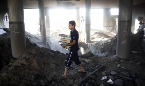 Bocah Palestina membawa buku agama yang ia selamatkan dari sebuah masjid di Gaza setelah serangan Israel, Sabtu (9/8)