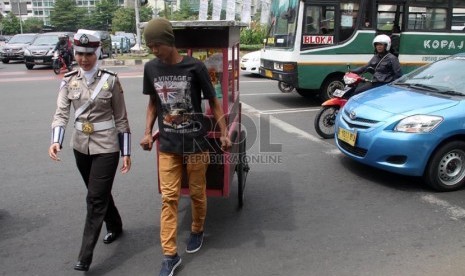  Bripka Novi dengan mengenakan seragam polisi berjilbab membantu pedagang menyeberang jalan di lampu merah Bundaran HI, Jakarta Pusat, Senin (25/11).  (Republika/Yasin Habibi)