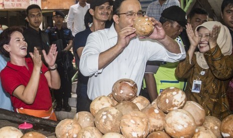 Calon Gubernur DKI Jakarta Anies Baswedan (tengah) meminum air kelapa saat kampanye di tengah pasar 