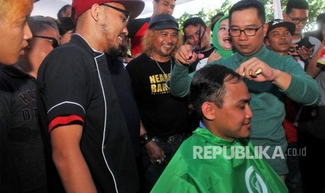 Calon Gubernur Jawa Barat Ridwan Kamil (kanan) secara simbolis mencukur warga pada acara pemecahan rekor Muri cukur rambut gratis 2.500 kepala, di Bekasi, Jawa Barat, Ahad (18/2). 