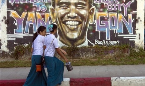 Myanmar university students walk past a graffiti of US President Barack Obama on a roadside in Yangon, Myanmar Friday, Nov. 14, 2014.