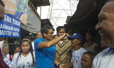 Cawagub DKI Jakarta nomor urut tiga Sandiaga Uno (tengah) memberi topinya kepada warga saat berkampanye di Kampung Kebon Bayam Taman BMW Jakarta, Rabu (25/1). 