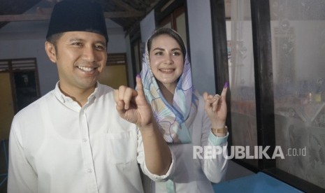 Cawagub Jatim Emil Elestianto Dardak (kiri) didampingi istri, Arumi Bachsin, menunjukkan bekas tinta pada ujung jari kelingking tanda telah menyalurkan hak pilih (mencoblos) di TPS 05 Kelurahan Ngantru, Trenggalek, Jawa Timur, Rabu (27/6). 