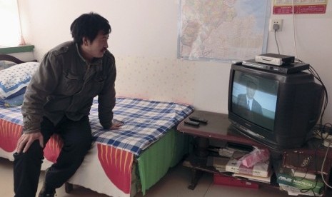  Chen Yongjiang, a fruit and vegetable farmer, sits on a bed as he watch a live broadcast of China's new Communist Party General Secretary Xi Jinping speaking during a media event to introduce the newly elected China's Politburo Standing Committee members,