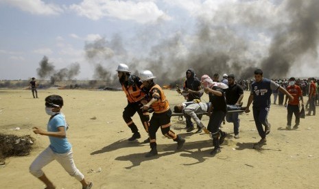 Dalam foto dokumentasi tanggal 14 Mei 2018 ini, petugas medis Palestina dan pengunjuk rasa mengevakuasi seorang pemuda yang terluka selama berlangsungnya protes di perbatasan Jalur Gaza dengan Israel, di sebelah timur Khan Younis, Jalur Gaza. Negara-negara Arab dengan tegas mengutuk pembunuhan lebih dari 50 warga Palestina pada Senin, 14 Mei 2018 dalam protes Gaza.