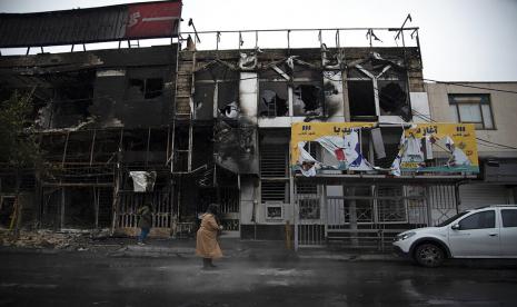 Dalam foto yang diambil pada 18 November 2019, dan dirilis oleh Kantor Berita Pelajar Iran, ISNA, orang-orang berjalan melewati gedung-gedung yang terbakar selama protes menyusul keputusan pihak berwenang untuk menaikkan harga bensin, di Karaj, sebelah barat ibu kota Teheran, Iran . Media pemerintah Iran mengatakan pihak berwenang telah menjatuhkan hukuman mati kepada lima orang karena diduga membunuh pasukan paramiliter yang berafiliasi dengan elit Pengawal Revolusi Islam Iran. Sebelas lainnya menerima hukuman penjara yang panjang. Ke-13 pria dan tiga anak di bawah umur itu dituduh membunuh pejabat dari Basij, cabang sukarelawan paramiliter IRG. Demikian menurut laporan Selasa, 6 Desember 2022 dari IRNA, kantor berita negara Iran.