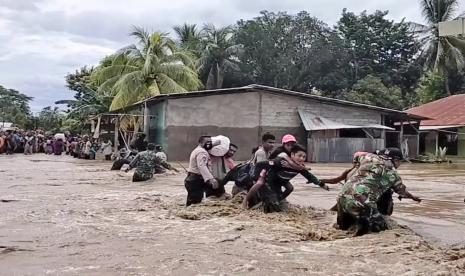 Dalam gambar yang dibuat dari video ini, tentara dan polisi membantu warga melintasi jalan banjir di Malaka Tengah, Provinsi Nusa Tenggara Timur, Indonesia, Senin, 5 April 2021. Berbagai bencana akibat hujan lebat di kawasan timur Indonesia telah menewaskan puluhan orang. tewas dan hilang serta ribuan orang mengungsi, kata badan bantuan bencana negara itu, Senin.