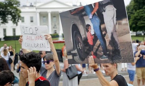 Demonstran memegang tulisan dan foto saat protes menentang kebijakan imigrasi Presiden Donald Trump yang memisahkan anak-anak dari orang tuanya di depan Gedung Putih, Kamis (21/6). Terdapat foto yang dijadikan sampul majalah Time edisi Juli 2018.