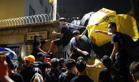 Demonstran menggunakan payung dan cat semprot saat mengepung markas polisi di Hong Kong, Kamis dini hari (27/6).