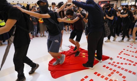 Demonstran menginjak bendera nasional China dalam protes di sebuah mal di Hong Kong, Ahad (22/9). 