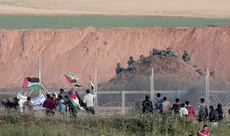 Demonstran Palestina melambaikan bendera di hadapan tentara Israel di perbatasan Gaza-Israel dekat Beit Lahiya, Rabu, 4 April 2018.