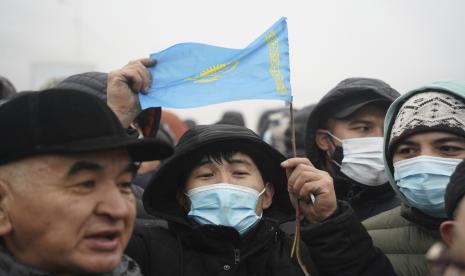 Demonstran, salah satunya memegang bendera nasional, berkumpul di dekat garis polisi selama protes di Almaty, Kazakhstan, Rabu, 5 Januari 2022.