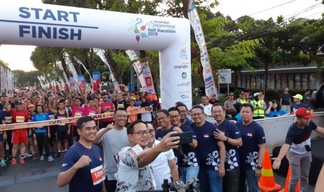 Direktur Utama Bank Mandiri Kartika Wirjoatmodjo dan Bupati Banyuwangi Abdullah Azwar Anas selfie di depan peserta Mandiri Banyuwangi Half Marathon 2019, di Banyuwangi, Ahad (31/3).