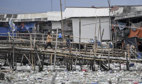 Dua anak berjalan meniti jembatan bambu yang penuh sampah di sekitarnya, di kawasan Kalibaru, Cilincing, Jakarta Utara, Rabu (8/6/2022). Pemprov DKI akan melibatkan seluruh RW di Jakarta ke dalam program sadar sampah.