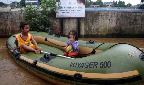 Dua anak bermain genangan air banjir dengan menaiki perahu karet di kelurahan Bukit Duri, Jakarta, Selasa (8/3).