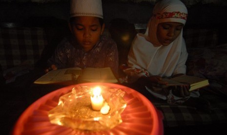 Dua anak membaca Alquran menggunakan penerangan lilin