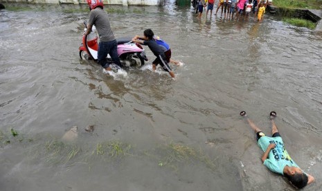  Dua bocah membantu mendorong motor yang mogok ketika melintasi banjir di Syech Yusuf Sungguminasa, Gowa, Sulsel, Selasa (24/12).