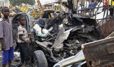 Dua bocah Nigeria berdiri dekat bangkai mobil bekas serangan bom yang diduga dilakukan oleh Boko Haram.