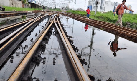 Dua calon penumpang melintasi rel yang tergenang di Kawasan Stasiun Kampung Bandan, Jakarta Utara, Selasa (15/1). 