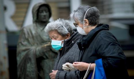 Dua manula berjalan mengenakan masker di Ourense, sebelah barat laut Spanyol, pada Sabtu (21/3). Akibat Covid-19 manula ditemukan meninggal dan terabaikan di Spanyol. 