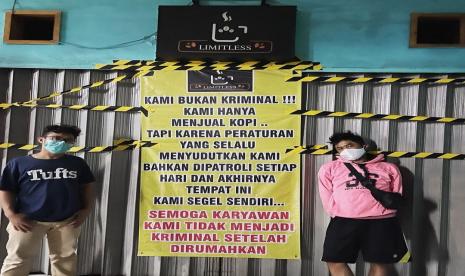 Dua orang berfoto di depan kafe Limitless Coffee di Jalan Raya Kebayoran Lama, Kelurahan Sukabumi Utara, Kebon Jeruk, Jakarta Barat. Pemilik kafe itu menyegel sendiri tempatnya berjulan karena merasa lelah selalu dirazia Satpol PP. 