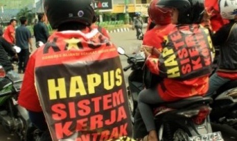 Dua orang buruh yang tergabung dalam Federasi Serikat Pekerja Karawang menempelkan poster berisi tuntutan menghapus sistem kerja kontrak pada kaosnya, saat unjuk rasa memperingati Hari Buruh Internasional, di Bundaran Mega M, Karawang, Jabar, Minggu (1/5).