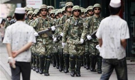 Dua orang Muslim Uighur di Xinjiang melintas di depan parade militer Cina.