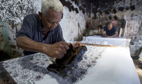 Pengrajin batik mengecap lilin (malam) ke atas kain di salah satu rumah di Centra Batik Tulis Trusmi, Desa Trusmi Wetan, Plered, Cirebon, Jawa Barat. Ada tiga desa di Kecamatan Plered saat ini menerapkan PSBM setelah 16 warga dinyatakan positif Covid-19. (ilustrasi)