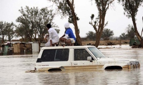   Dua orang pria duduk diatas mobil mereka yang terendam banjir setelah hujan lebat di Tabuk, Arab Saudi, Senin (28/1).   (Reuters/Mohamed Alhwaity)