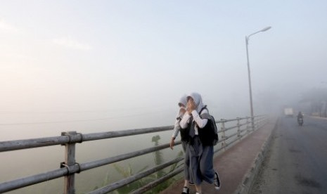 Dua orang siswa pelajar melewati kabut asap yang menutupi di jembatan Musi II, Palembang. Sumsel. Senin (31/8). 