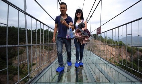 Dua orang wisatawan tengah berjalan di jembatan gantung yang terbuat dari kaca di Cina