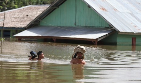 Dua warga menerobos banjir yang terjadi di Desa Tonduno, Konawe Selatan, Sulawesi Tenggara, Senin (17/6/2019). 