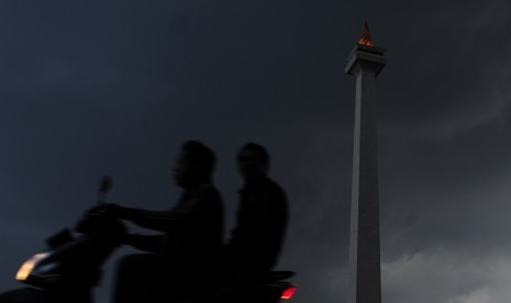 Dua warga mengendarai sepeda motor melintasi Monas yang diselimuti awan hitam di Kawasan Monas, Jakarta, Senin (30/11). 