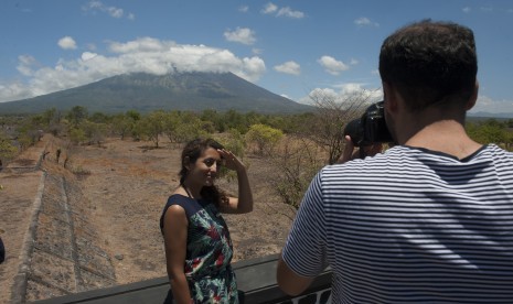 Dua wisatawan berfoto dengan latar belakang Gunung Agung, di Desa Batu Niti yang berjarak sekitar 12 kilometer dari gunung berstatus awas itu, Karangasem, Bali, Senin (25/9). 