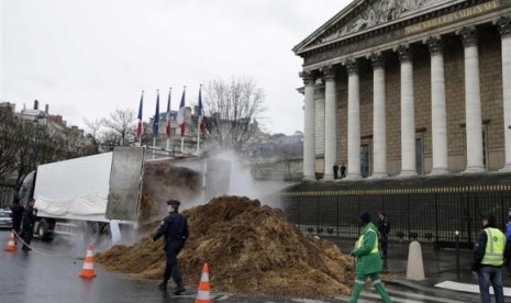 French police and municipal workers walk near a large pile of manure sitting in front of the National Assembly in Paris January 16, 2014.