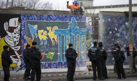 German police officers protect a part of the former Berlin Wall in Berlin, Germany, Friday, March 1, 2013. Berliners are protesting as a construction company removes a section of a historic stretch of the Berlin Wall known as the East Side Gallery to provi