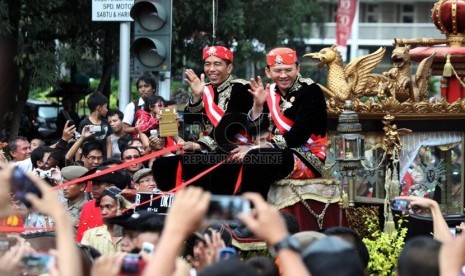   Gubernur DKI Jakarta Joko Widodo dan Wakil Gubernur Basuki Tjahaja Purnama menyapa warga diatas kereta kencana saat mengikuti kirab di Jalan Medan merdeka Barat, Jakarta, Ahad (8/12).  (Republika/Yasin Habibi)