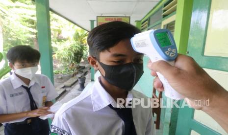 Guru mengukur suhu tubuh siswa sebelum memasuki ruang kelas saat pembelajaran tatap muka terbatas (PTMT) di SMP N 1 Ngasem, Kediri, Jawa Timur, Selasa (14/9/2021). Sejumlah sekolah jenjang pendidikan SD dan SMP di Kabupaten Kediri mulai menyelenggarakan PTMT yang diikuti maksimal 50 persen siswa dengan menerapkan protokol kesehatan COVID-19. 