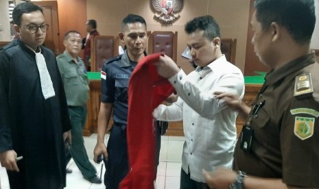 Haris Simamora sedang memasang kembali rompinya untuk keluar dari ruang sidang Pengadilan Negeri Bekasi, Selasa (31/7). Terdakwa kasus pembunuhan satu keluarga ini dijatuhi hukuman pidana mati oleh majelis hakim.