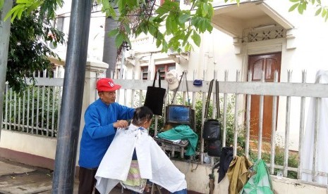 Hasanudin sedang merapikan rambut pelanggannya. Hasan merupakan satu-satunya tukang cukur DPR yang tersisa di kawasan sekitar Jatinegara.