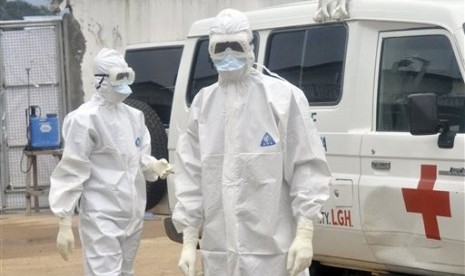 Health workers wearing protective gear wait to carry the body of a person suspected to have died from Ebola, in Monrovia, Liberia, Monday Oct. 13, 2014. 