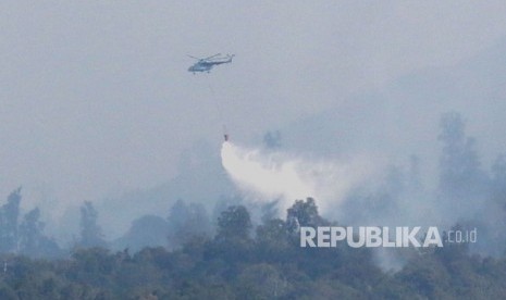 Helikopter melakukan water bombing di atas hutan yang terbakar, ilustrasi