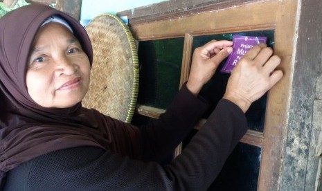 Ibu Keni sedang menempelkan stiker Amartha di warung nasi uduk miliknya