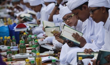 Ilustrasi Seorang anak membaca Al-quran saat menunggu waktu berbuka puasa bersama.