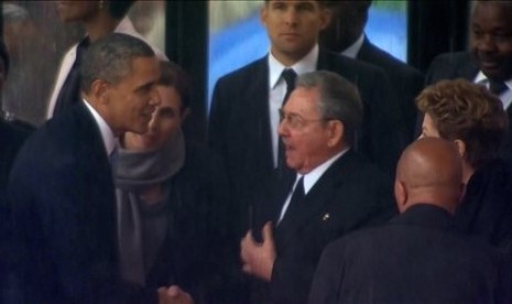 In this image from TV, US President Barack Obama shakes hands with Cuban President Raul Castro at the FNB Stadium in Soweto, South Africa, in the rain for a memorial service for former South African President Nelson Mandela, Tuesday Dec. 10, 2013. 