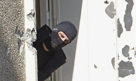 In this March 23, 2014 file photo, a masked police officer searches for clues at terrorist Mohamed Merah's apartment building in Toulouse, southern France. 