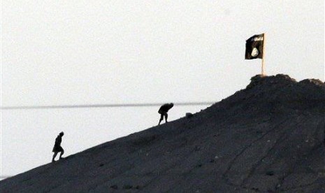 In this Oct. 6, 2014 file photo, shot with an extreme telephoto lens from the outskirts of Suruc at the Turkey-Syria border, militants with the Islamic State group are seen after placing their group's flag on a hilltop at the eastern side of Kobani, Syria.